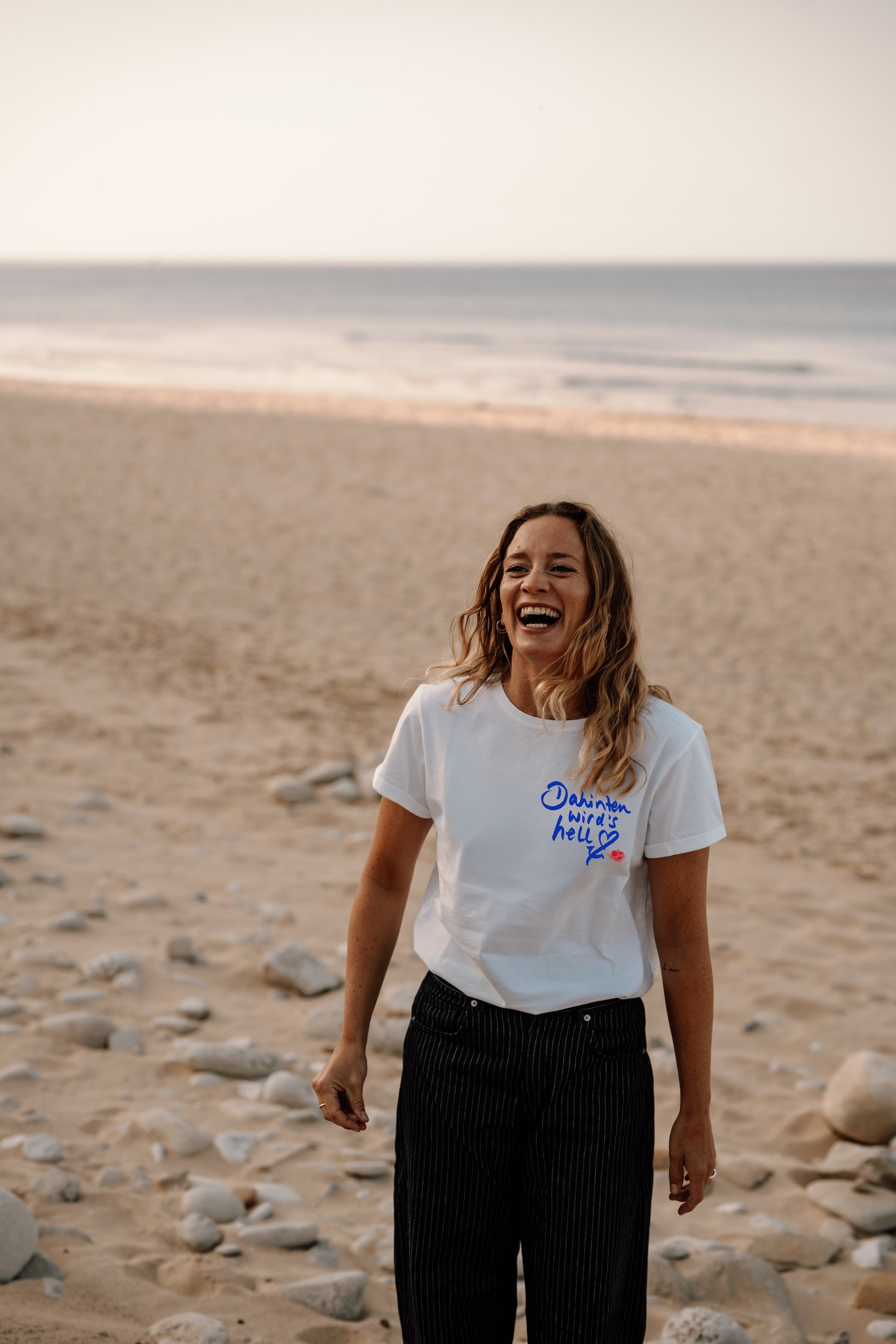 Frauen T-Shirt „Dahinten wird's hell" – weiß, Aufdruck in Blau, getragen am Strand | Ankerherz